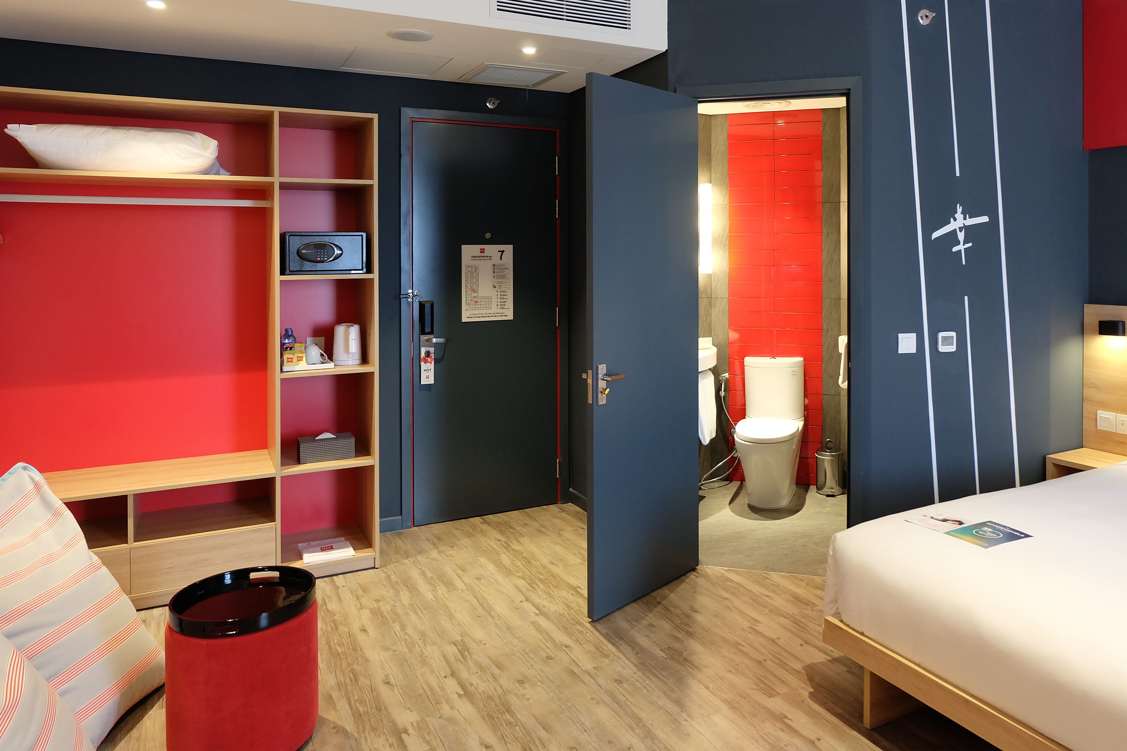 Ein Hotelzimmer mit einem Bett, einer roten Ablage, einem Holzboden und einer Tür zu einem Badezimmer mit roter Wand.