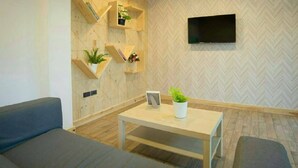 A modern living room with a sofa, a coffee table, and wooden shelves with plants. - Hughomestay Hotel (Ubon Ratchathani)