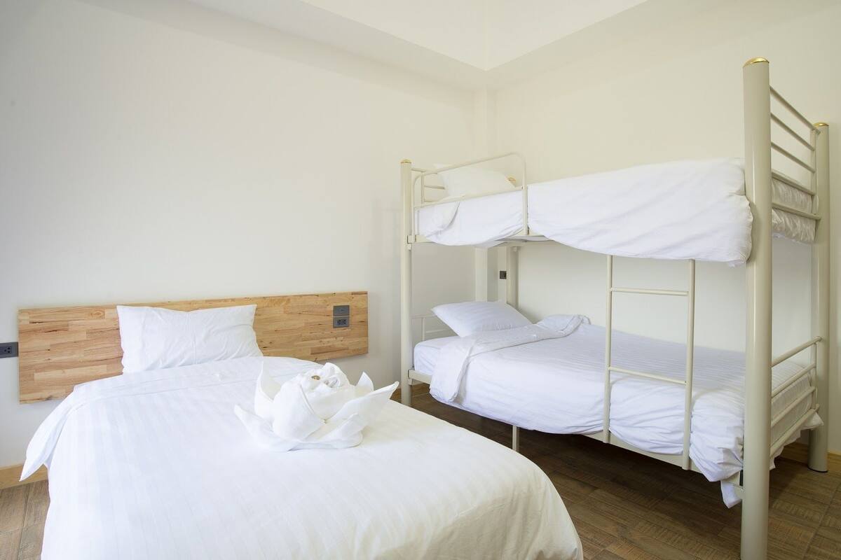 Una cama individual con cabecera de madera, una litera con ropa de cama blanca y un suelo de madera.