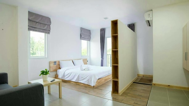 A modern bedroom with a bed, a small table with a plant, a grey armchair, and a wardrobe. - Hughomestay Hotel (Ubon Ratchathani)