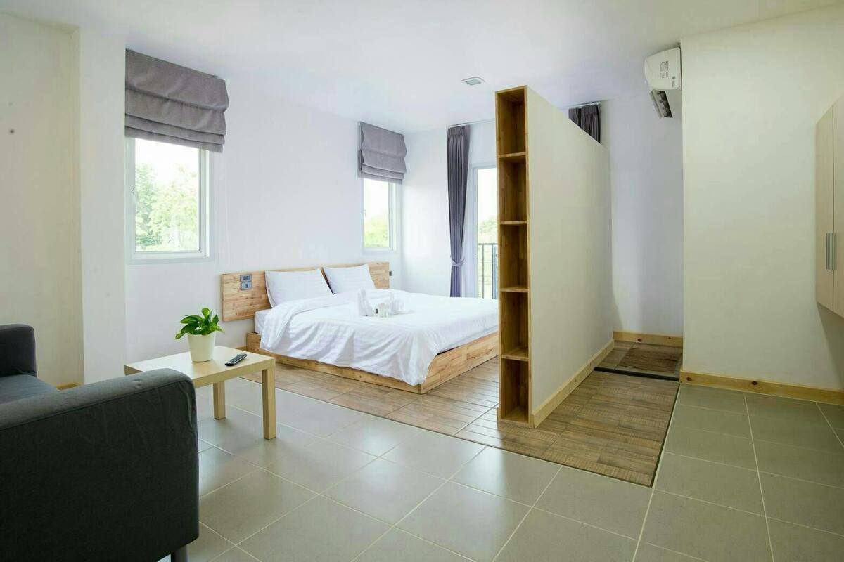 Un dormitorio moderno con una cama, una mesita con una planta, un sillón gris y un armario.