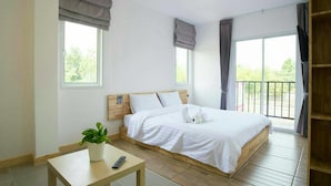 A bedroom with a wooden bed, a small table with a plant, a remote control, and a balcony with curtains. - Hughomestay Hotel (Ubon Ratchathani)