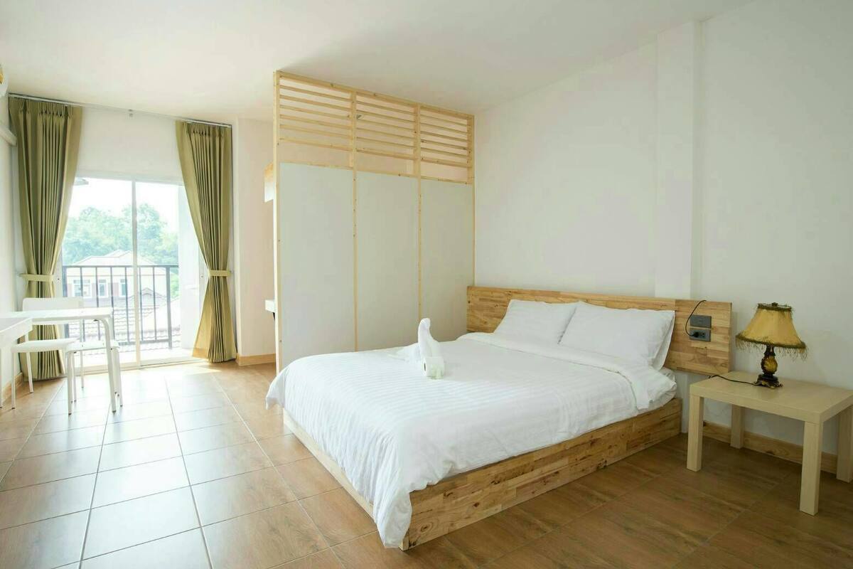 Un dormitorio con cama de madera, una mesita de noche con lámpara, una ventana con cortinas y una pequeña mesa con sillas.