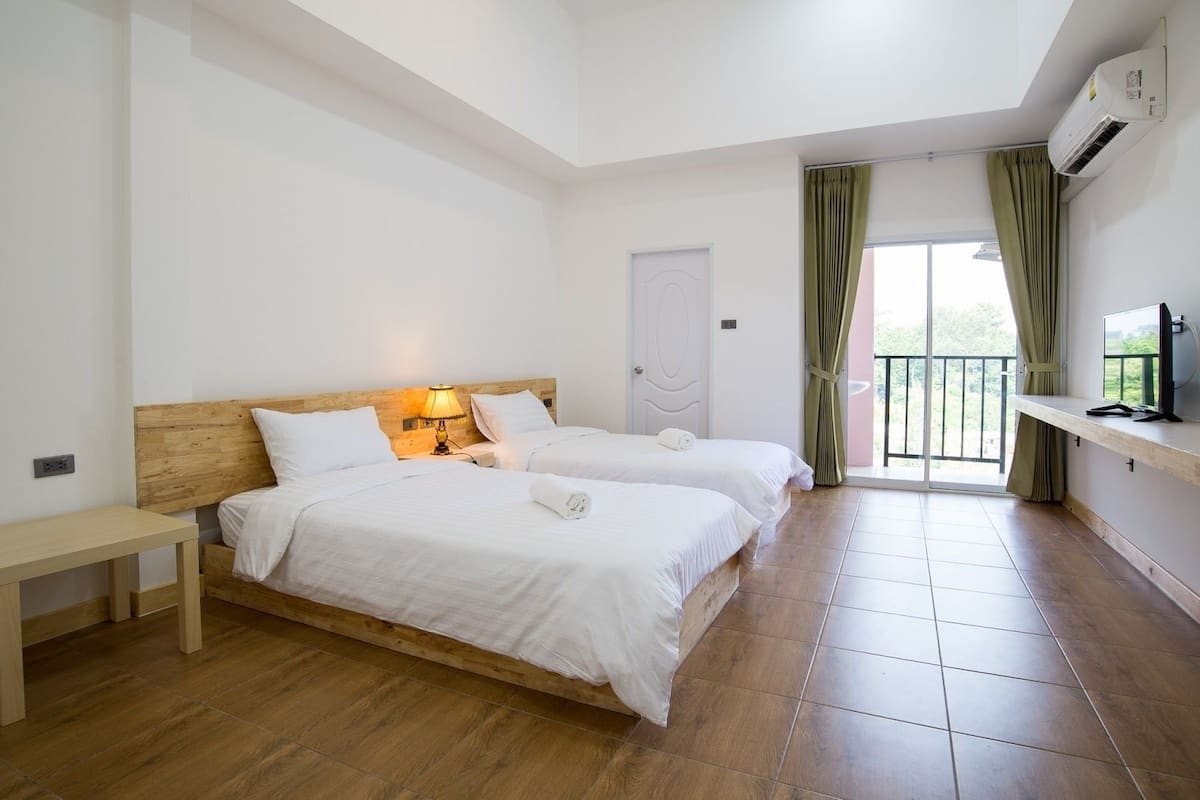 Habitación de hotel con dos camas, cabecera de madera, mesita de noche, televisor y balcón con cortinas.