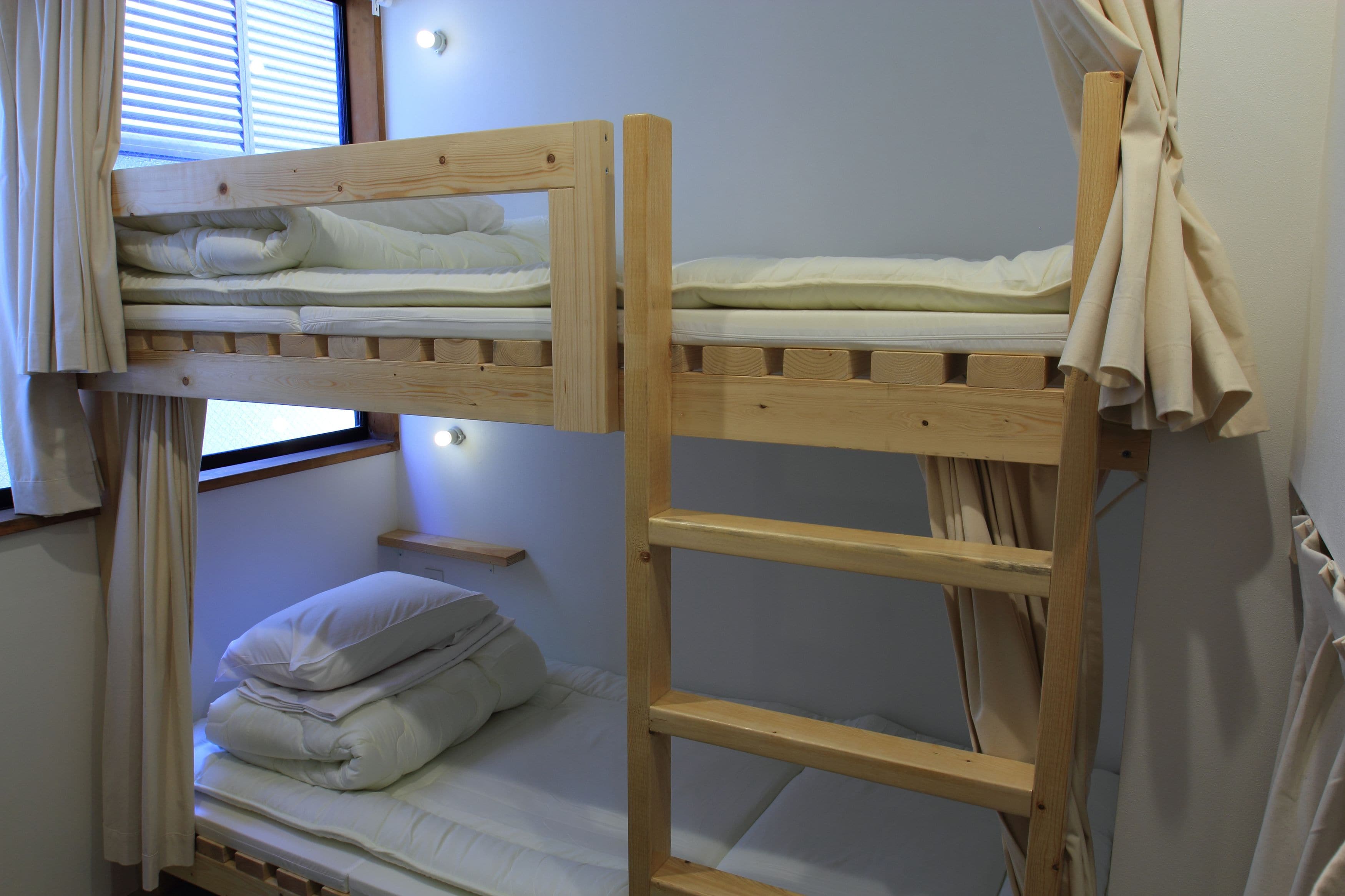 A bunk bed with a wooden frame, a lower single bed, and a window with blinds.