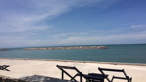 A beach with a concrete walkway, a rocky breakwater, and two empty lounge chairs facing the sea. - Chomtalay Resort at Had Chaosamran Beach (Ban Laem)