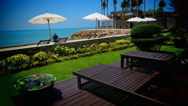 A deck with a pond, lounge chairs, and umbrellas overlooking a beach. - Chomtalay Resort at Had Chaosamran Beach (Ban Laem)