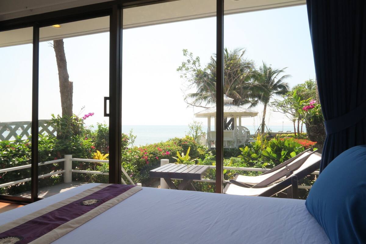 A bedroom with a bed, a view of the sea, and a balcony with plants and a table.