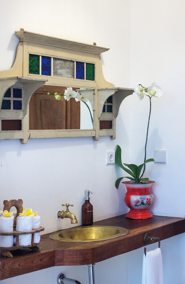 A bathroom with a wooden vanity, a brass sink, a mirror with stained glass, and a potted orchid. - Umakayu Bali (Canggu)