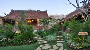 A traditional house with a tiled roof, surrounded by lush greenery and a stone pathway. - Umakayu Bali (Canggu)