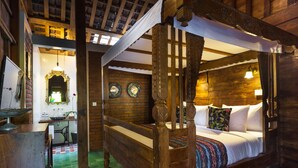 A rustic wooden four-poster bed with white linens and colorful pillows, a wooden desk with a mirror, and a green checkered floor. - Umakayu Bali (Canggu)