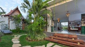 A courtyard with a stone pathway, palm trees, and a statue. - Umakayu Bali (Canggu)