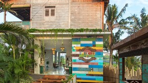 A traditional wooden house with a colorful mural, a stone pathway, and lush greenery. - Umakayu Bali (Canggu)