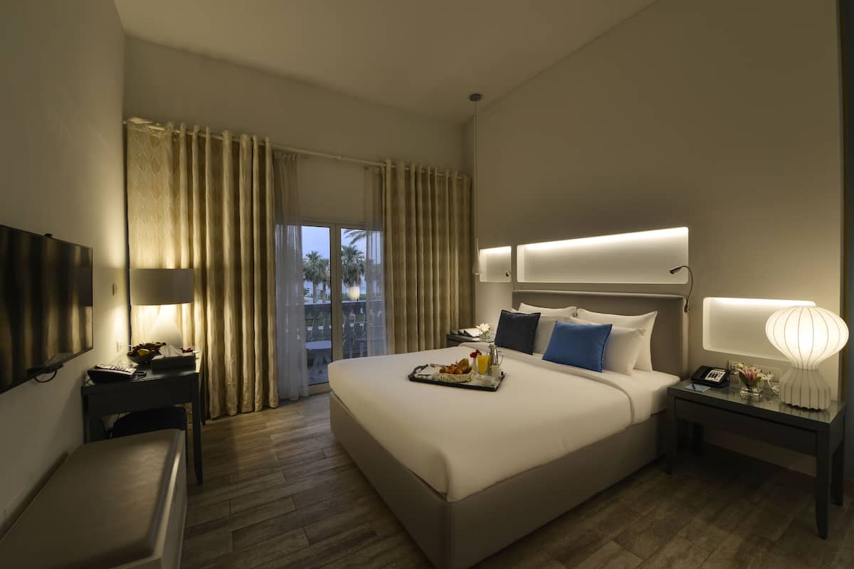 Quarto de hotel com uma cama grande, mesas de cabeceira, televisão e varanda com cortinas.