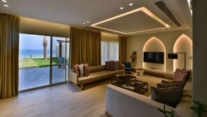 A spacious living room with a large sliding glass door leading to a balcony, a comfortable sofa, a coffee table, and a flat-screen TV mounted on the wall.