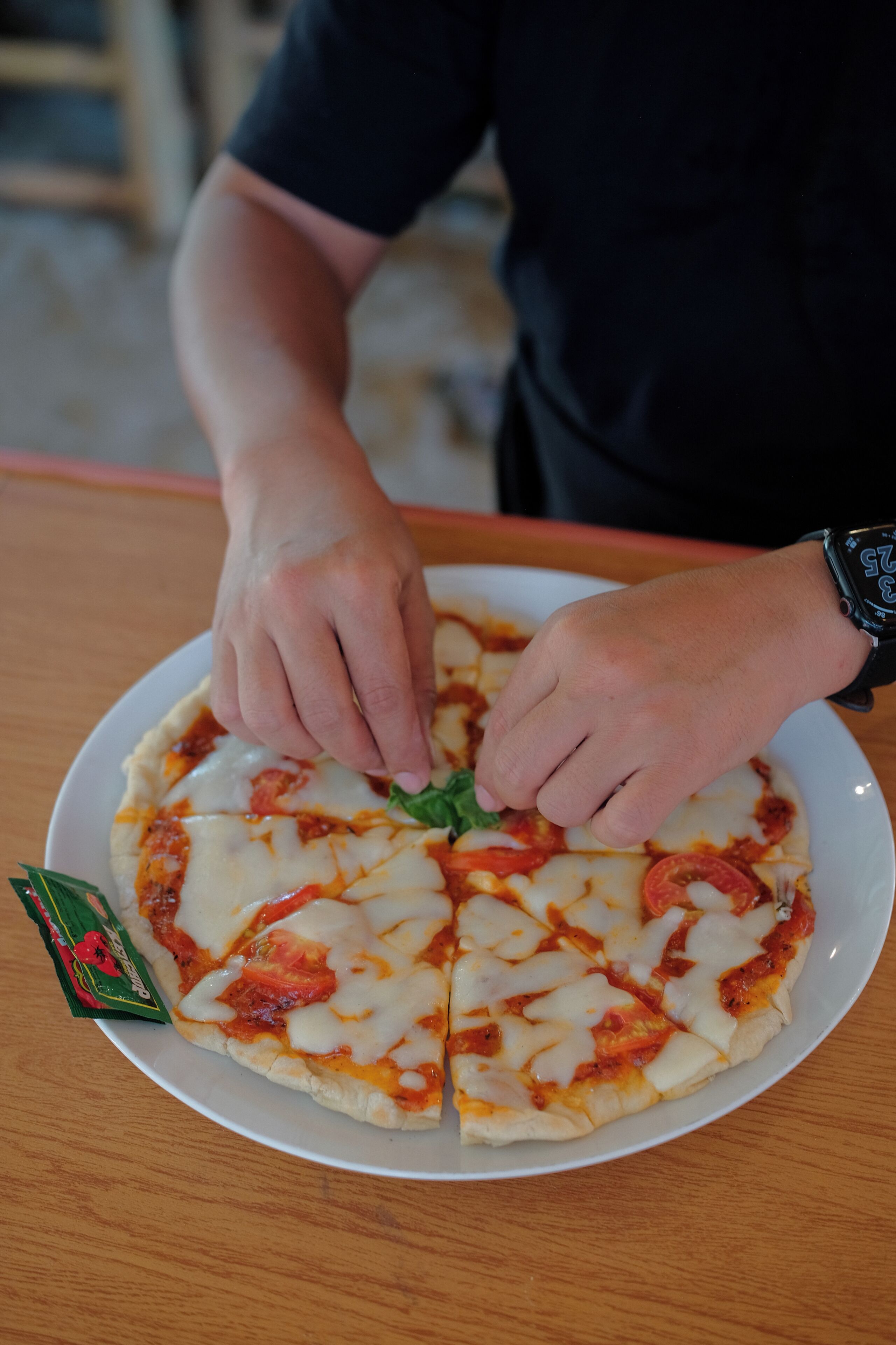 A person placing a green leaf on a pizza.