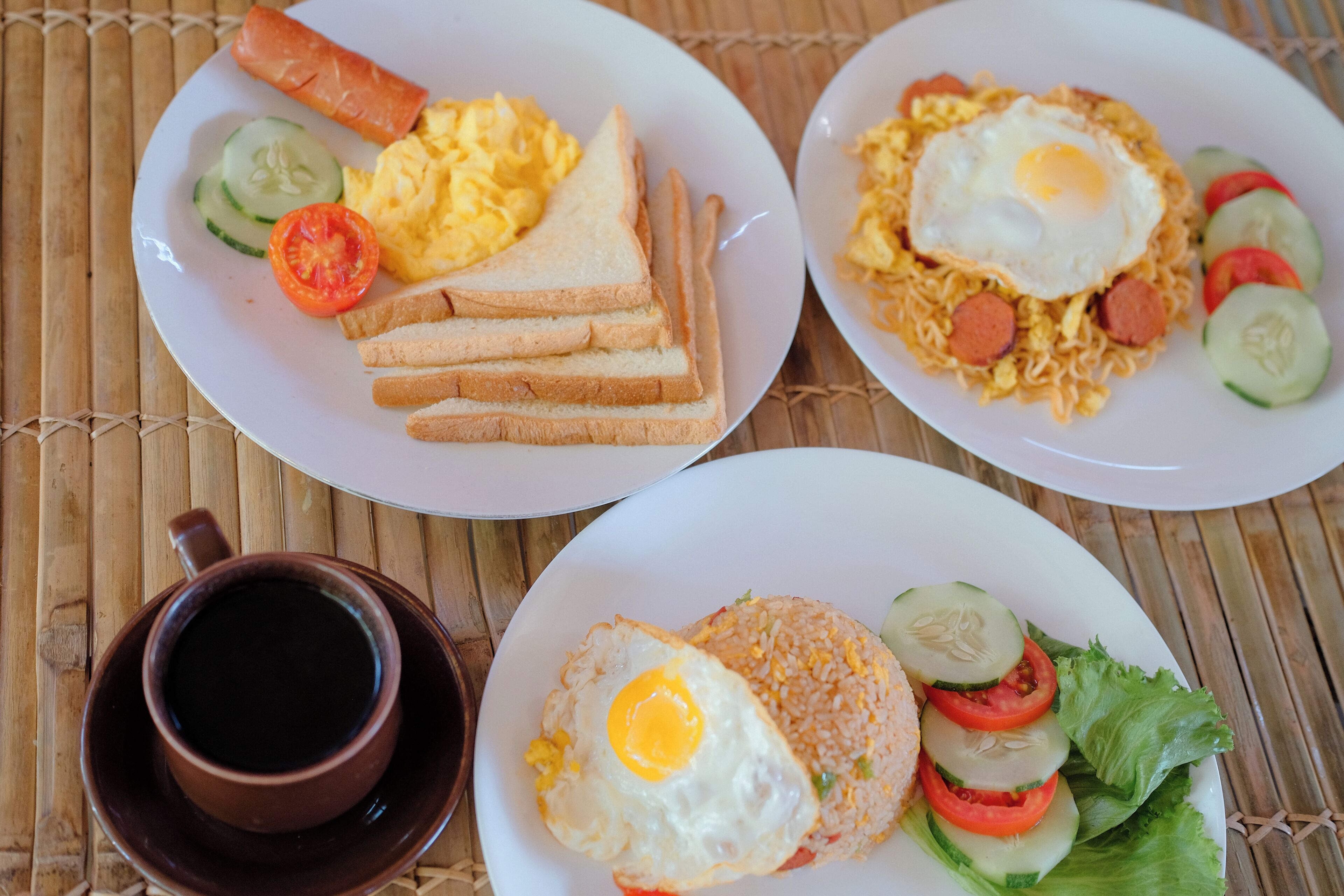 Tres platos de comida con una taza de café sobre una estera de bambú.