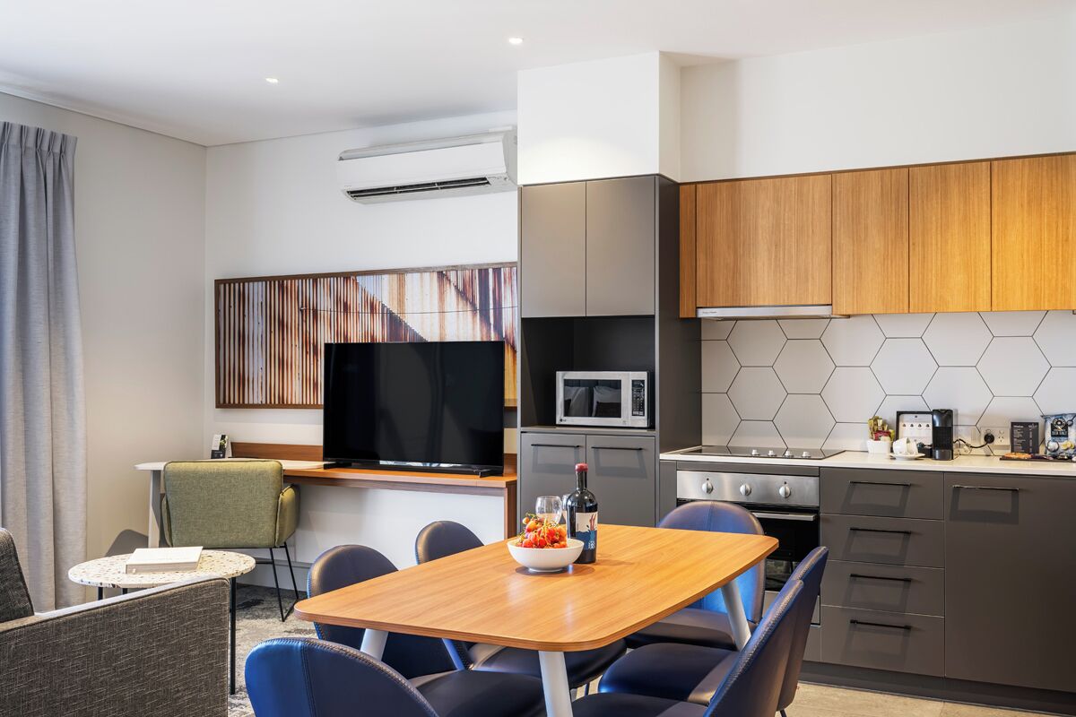 A modern kitchen with a microwave, stove, and wooden cabinets. There is a dining area with a table and chairs.