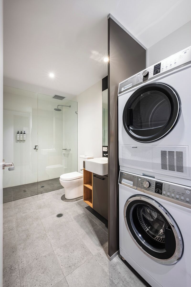 A modern bathroom with a glass shower enclosure, a toilet, a sink, and a stacked washer and dryer.