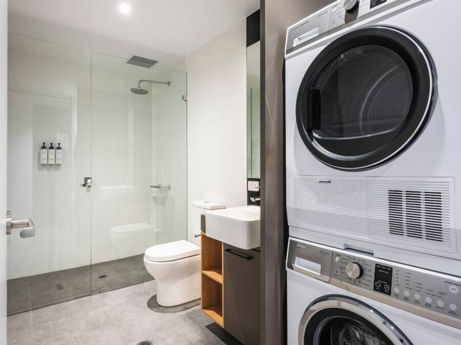 Un baño moderno con cabina de ducha de vidrio, inodoro, lavamanos y lavadora y secadora apiladas.