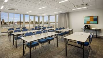 Une salle de conférence dotée de plusieurs tables et chaises, de grandes fenêtres offrant une vue sur l’extérieur et d’un plafond moderne agrémenté de luminaires.