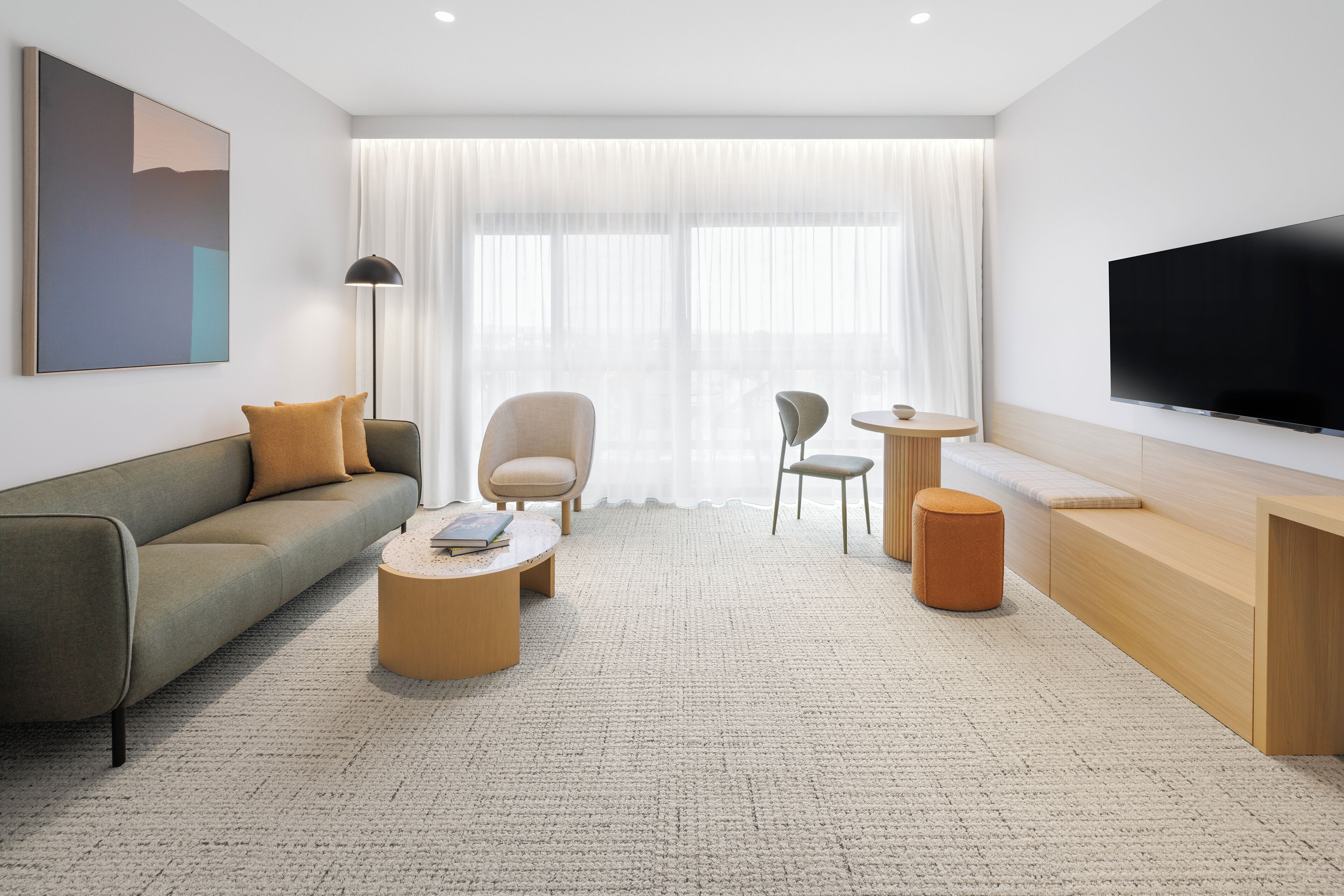 A modern living room with a sofa, coffee table, chairs, a TV, and a large window with sheer curtains.