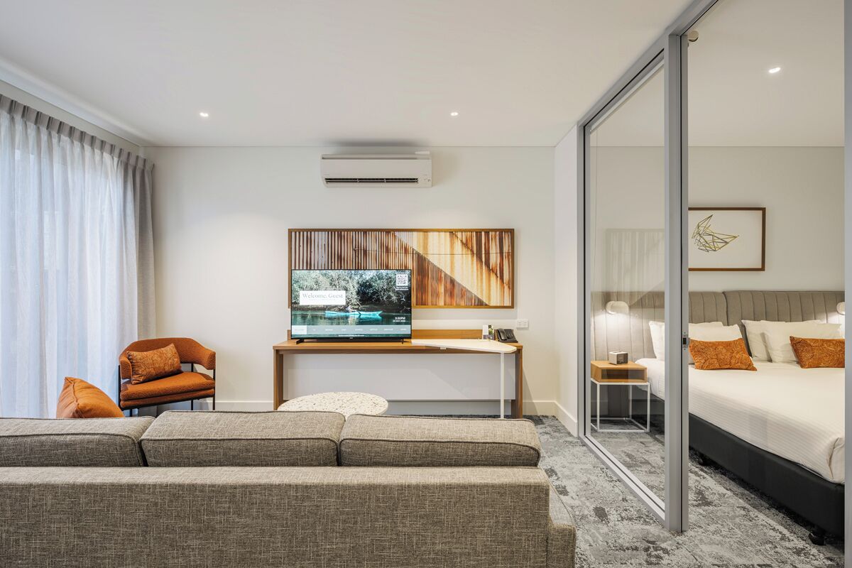 A modern hotel room with a sofa, a TV, a bed, and a sliding glass door.