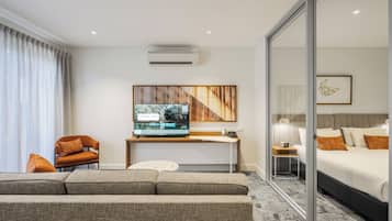 A modern hotel room with a sofa, a TV, a bed, and a sliding glass door.