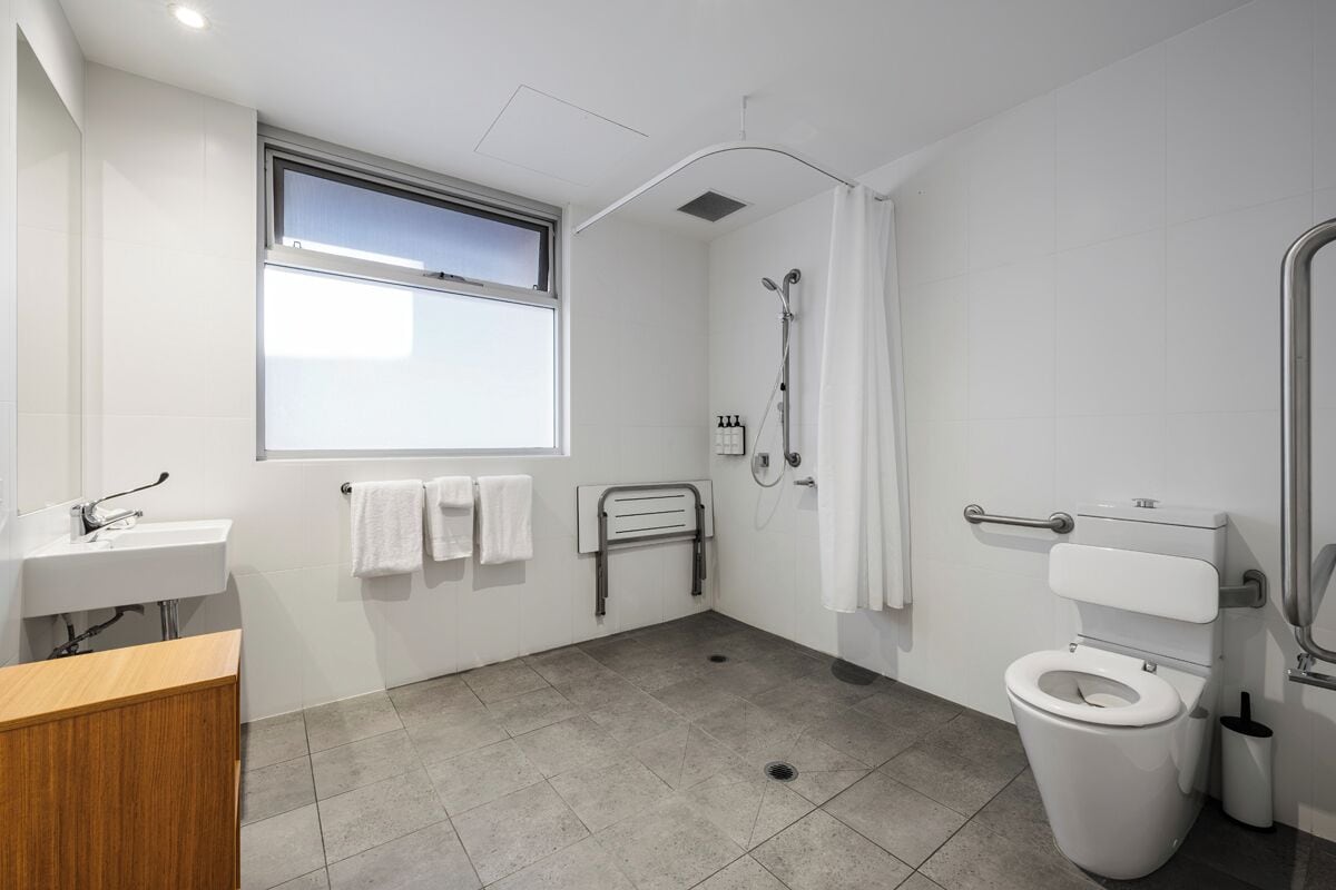 A modern bathroom with a shower, toilet, sink, and window.