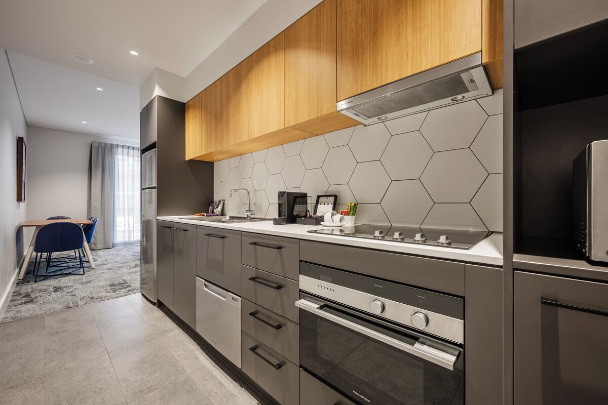 A modern kitchen with stainless steel appliances, wooden cabinets, and a hexagonal tile backsplash.