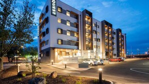 Un hôtel à plusieurs étages au design moderne, doté de balcons à chaque niveau et d’une entrée bien éclairée.