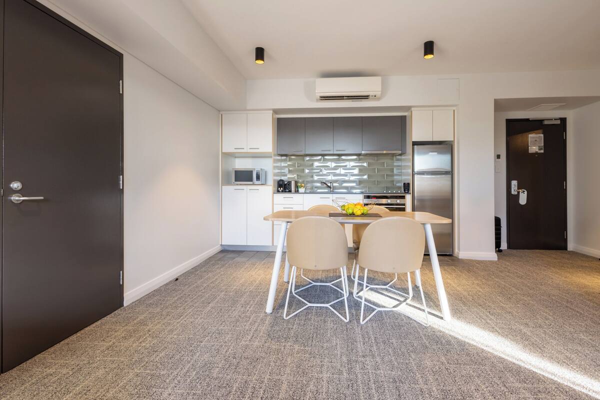 A compact kitchen with white cabinets, a microwave, a refrigerator, and a dining area with a table and chairs.
