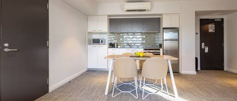 A compact kitchen with white cabinets, a microwave, a refrigerator, and a dining area with a table and chairs.