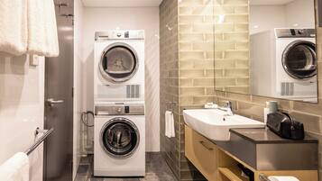 Un baño de hotel pequeño con dos lavadoras apiladas, un lavabo y un espejo.