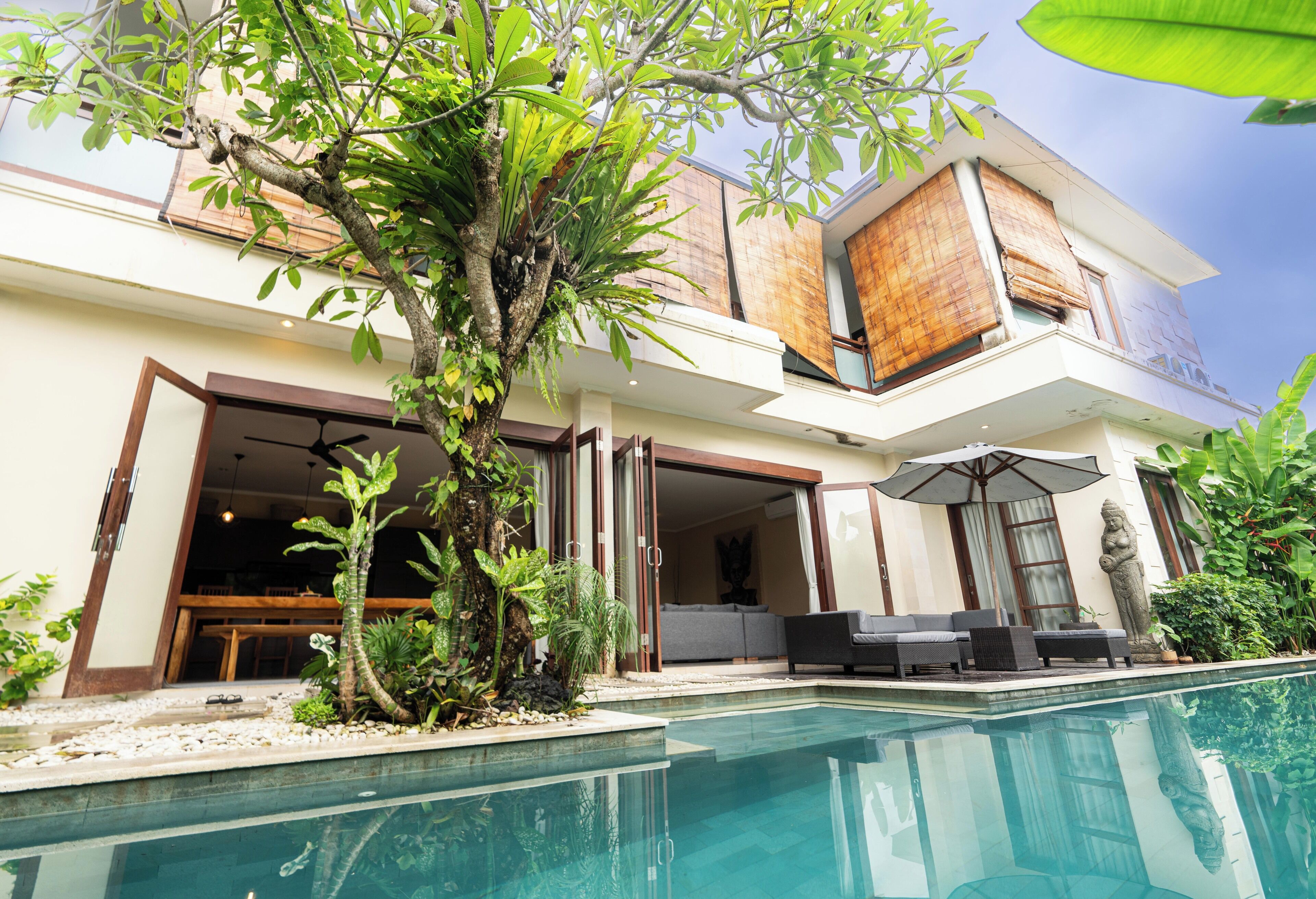 A modern house with a swimming pool, outdoor seating, and tropical plants.