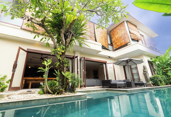 Una casa moderna con piscina, mobiliario exterior y plantas tropicales.