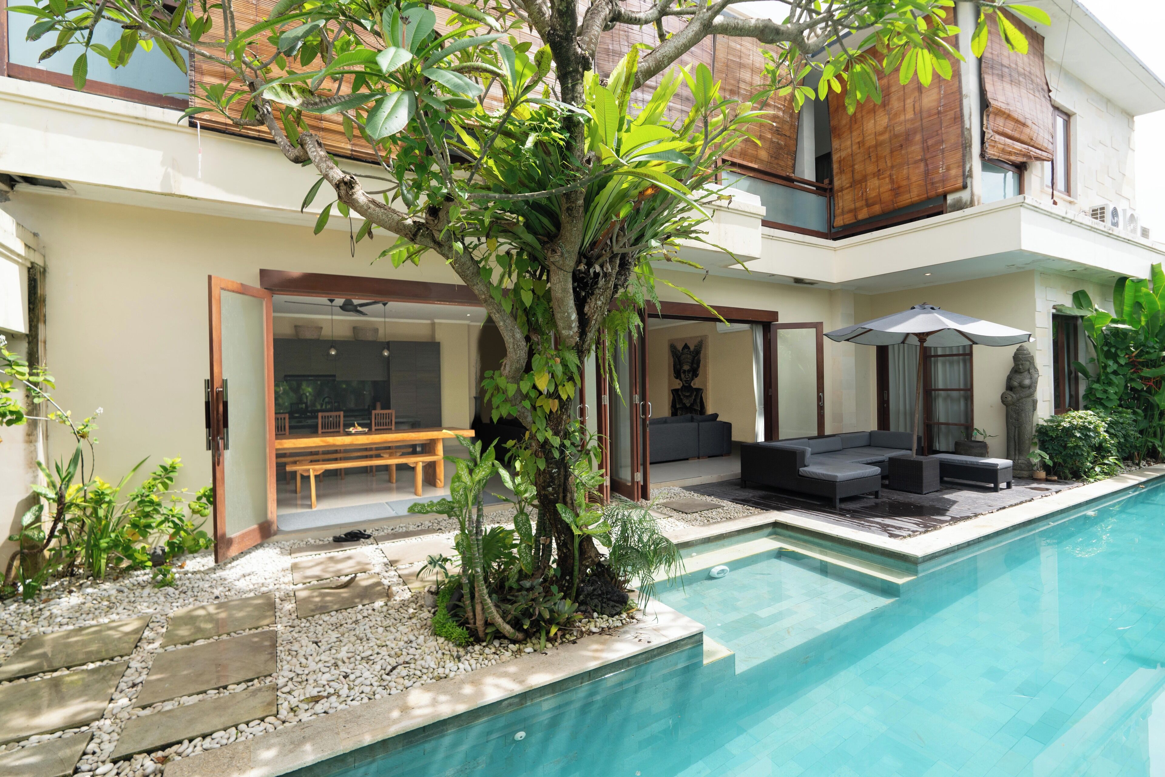 Una casa moderna con piscina, mobiliario exterior y abundante vegetación.