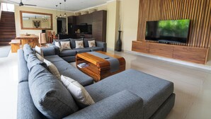 Una sala de estar moderna con un sofá seccional, una mesa de centro de madera y un televisor de pantalla plana montado en una pared de paneles de madera.