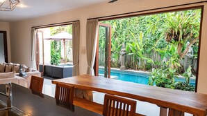 Una cocina moderna con una amplia mesa de madera, un lavamanos integrado y vistas a una piscina y exuberante vegetación.