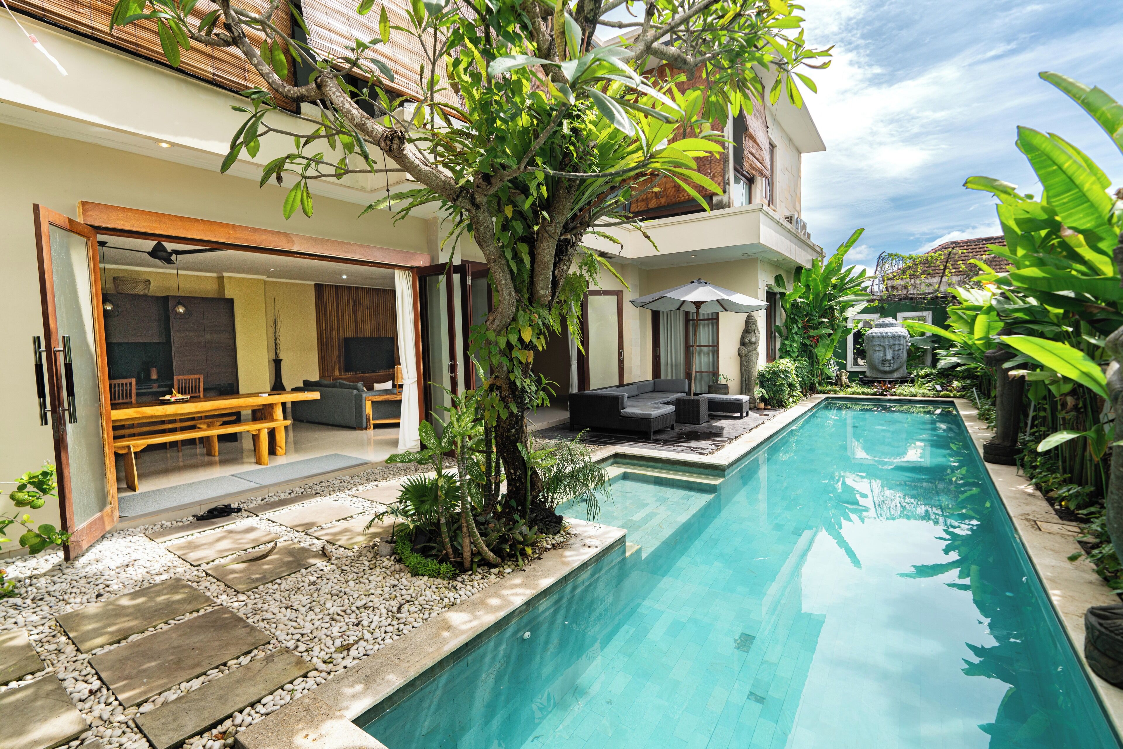 A swimming pool with a stone deck, surrounded by lush greenery and a modern outdoor seating area.