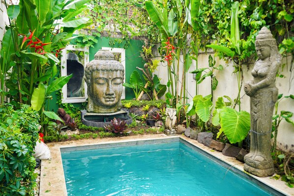 Un jardin paisible avec une piscine, entouré d’une végétation luxuriante et de statues.