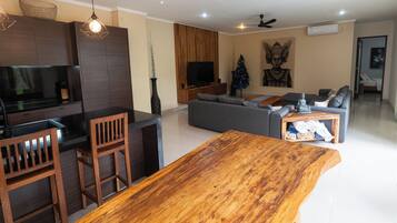 Un salón moderno con una mesa de comedor de madera, un sofá gris y un televisor montado en la pared.