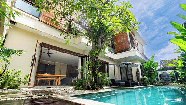 Una casa moderna con piscina, zona de comedor y un gran árbol en el patio trasero.