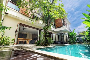 A modern house with a swimming pool, a dining area, and a large tree in the backyard. - Villa Tepi Sungai (Legian)