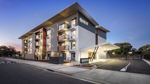 A modern multi-story building with a prominent "QUEST" sign, featuring balconies, a covered entrance, and a parking area. - Quest Griffith (Griffith)
