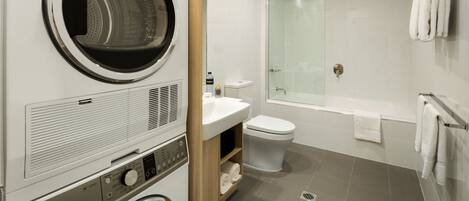 A modern bathroom with a built-in washer and dryer, a glass shower enclosure, and a white sink.