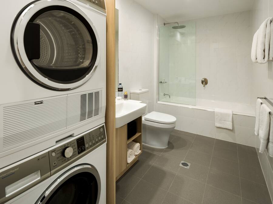 A modern bathroom with a built-in washer and dryer, a glass shower enclosure, and a white sink.