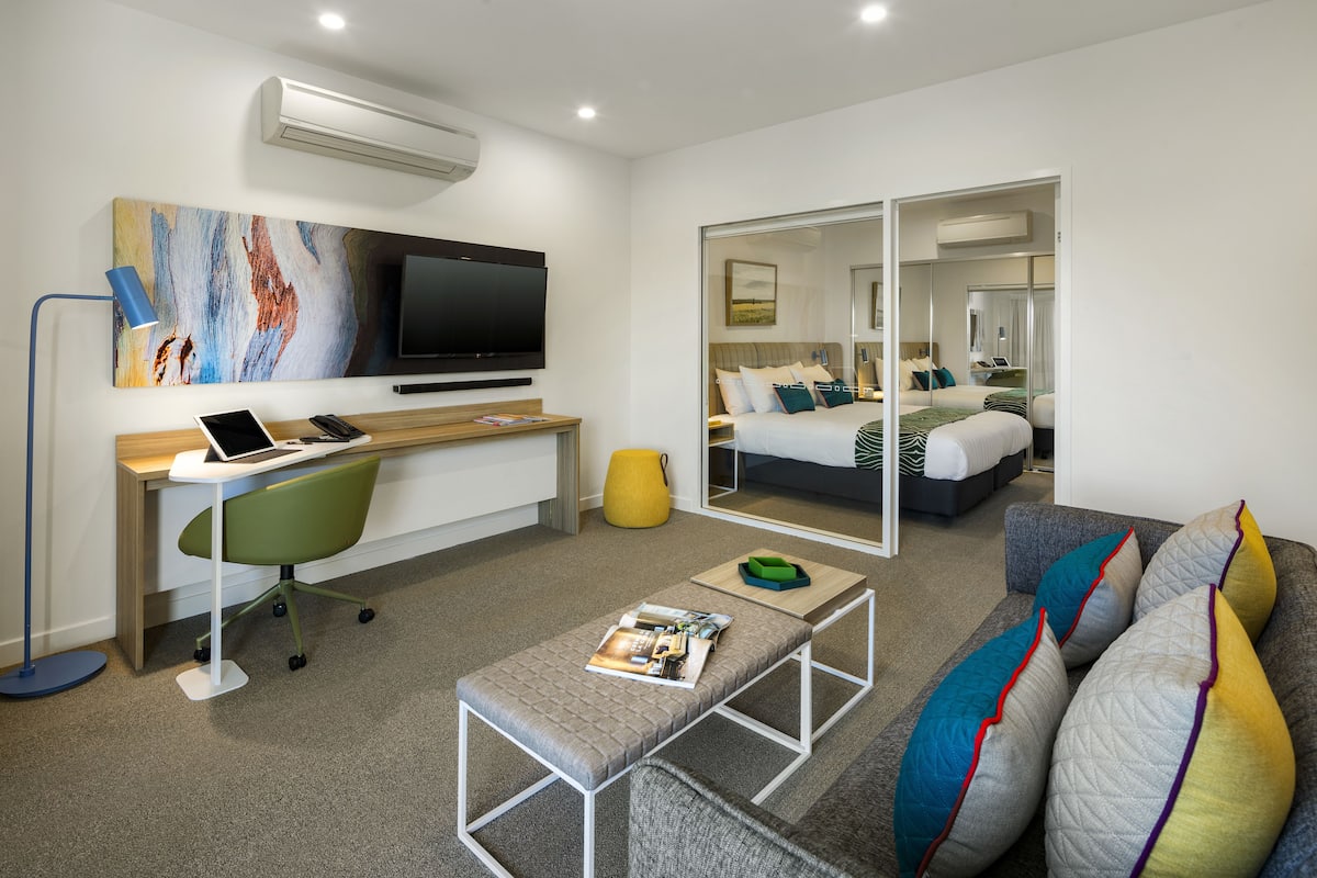 Una habitación de hotel moderna con escritorio, silla y cama con un espejo grande.