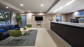 A modern reception area with a flat-screen TV, a reception desk, a green chair, a sofa with blue cushions, and a plant. - Quest Griffith (Griffith)