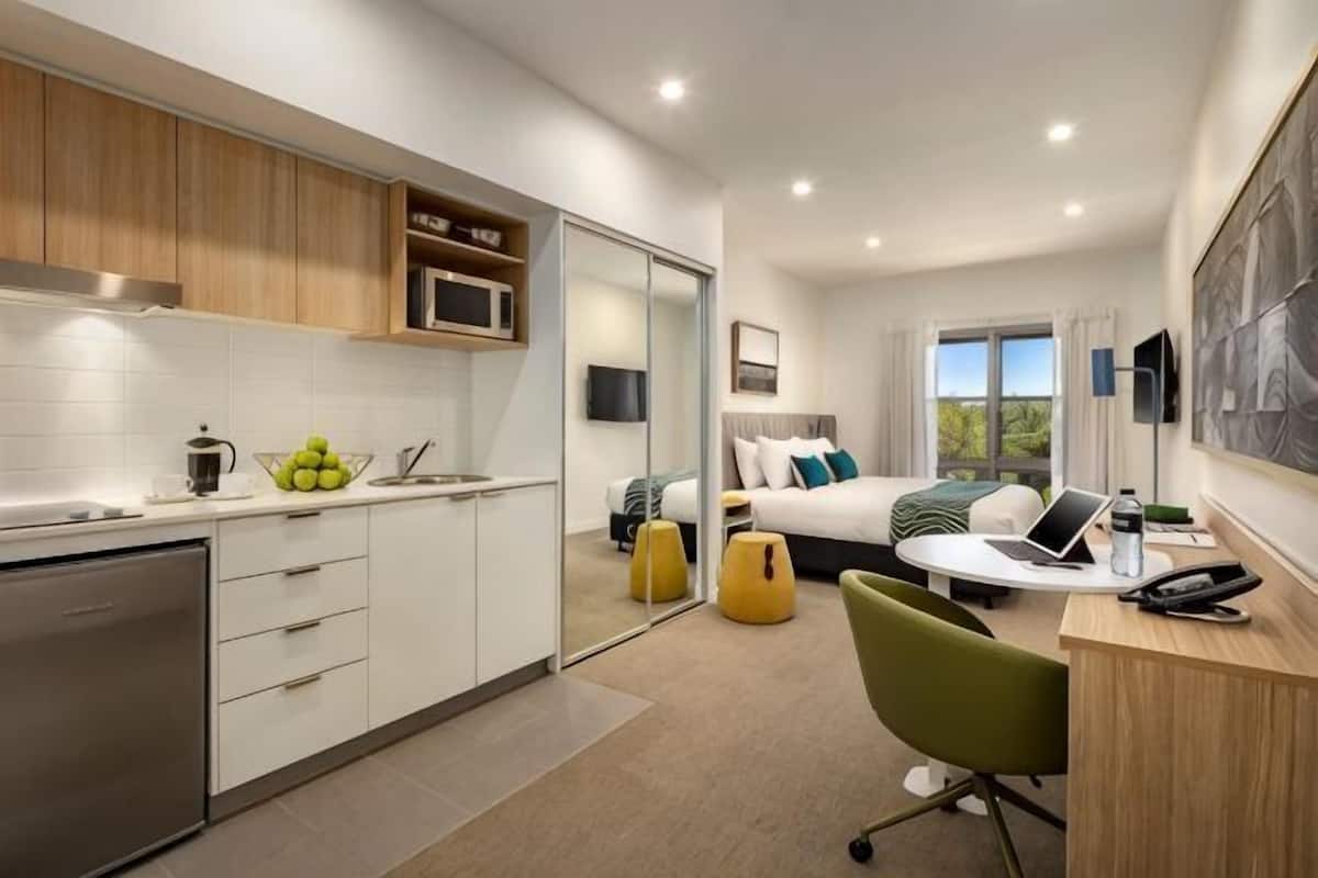 Una habitación de hotel moderna con kitchenette, una cama con vistas, un escritorio con silla y un ventanal grande.